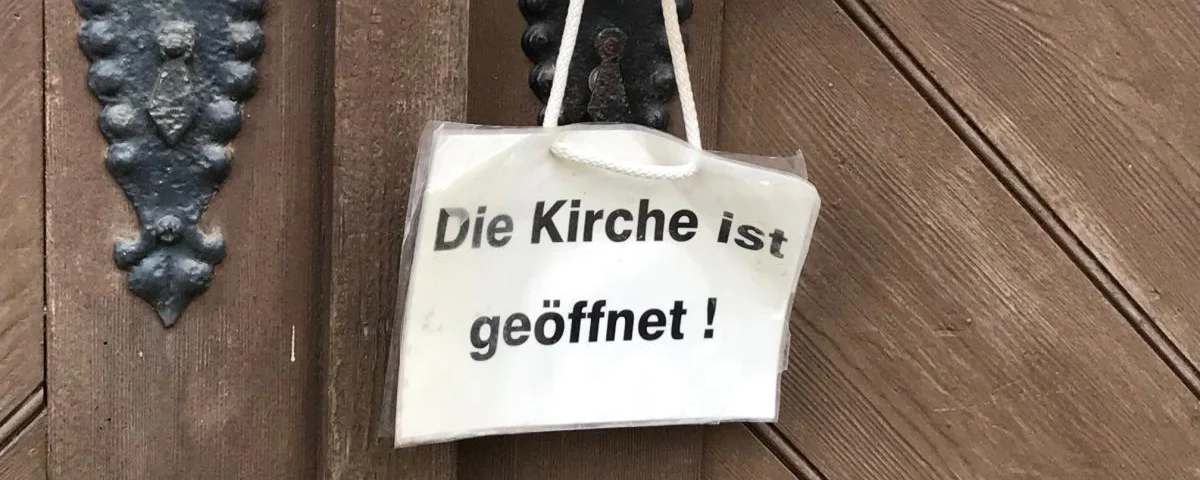 An einer Kirchentür hängt ein "Geöffnet"-Schild