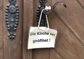 An einer Kirchentür hängt ein "Geöffnet"-Schild