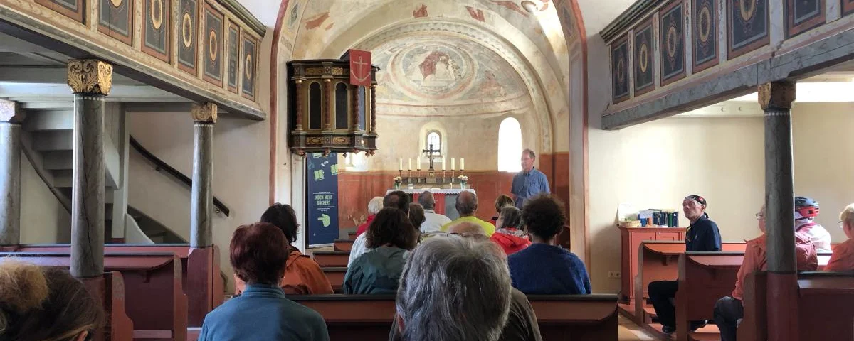 Blick in der Axiener Kirche von hinten nach vorne zum Altar, auf den Bänken sitzen Gottesdienstteilnehmer.