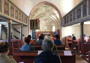 Blick in der Axiener Kirche von hinten nach vorne zum Altar, auf den Bänken sitzen Gottesdienstteilnehmer. | Foto: Privat