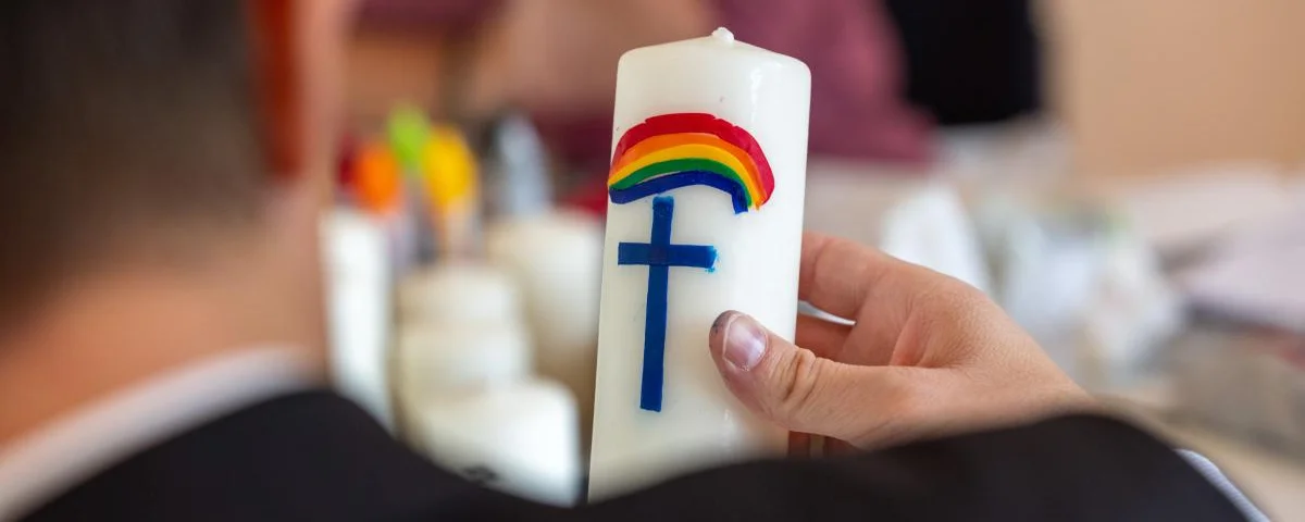 Taufkerze verziert mit einem Regenbogen und einem blauen Kreuz.